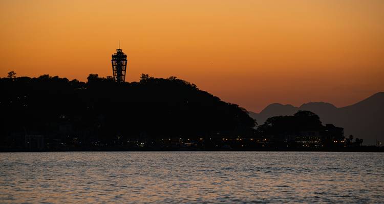 Silhouette d'une tour et de bâtiments au coucher du soleil au bord de l'eau.