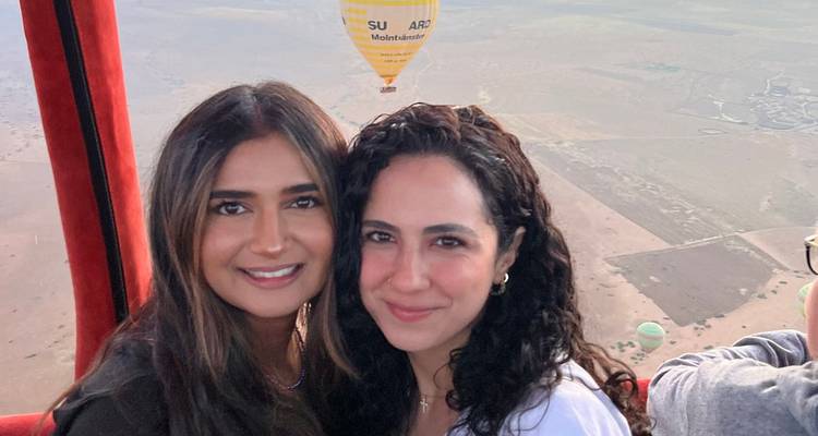 Deux femmes souriantes dans la nacelle d'une montgolfière avec des vues panoramiques en arrière-plan.