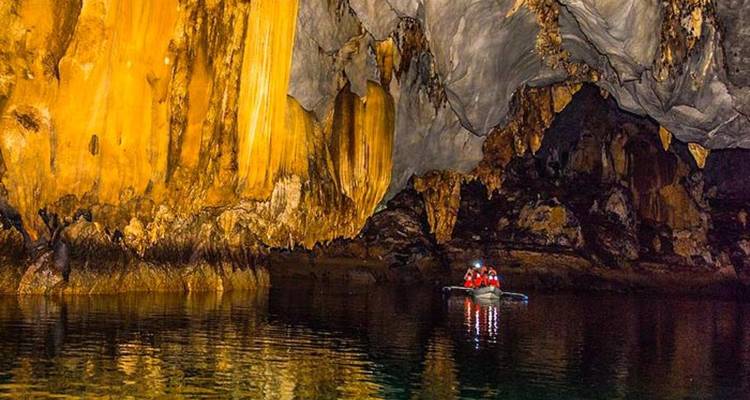 Tourists in a cave on a boat surrounded by stunning rock formations.