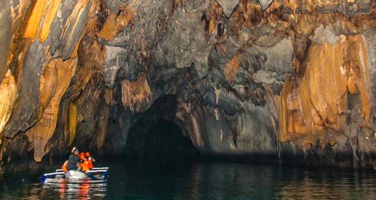 People in a boat exploring a large cave with impressive stalactites.