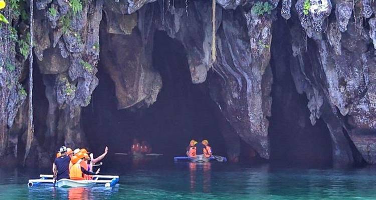 Boats navigating towards a large cave entrance.