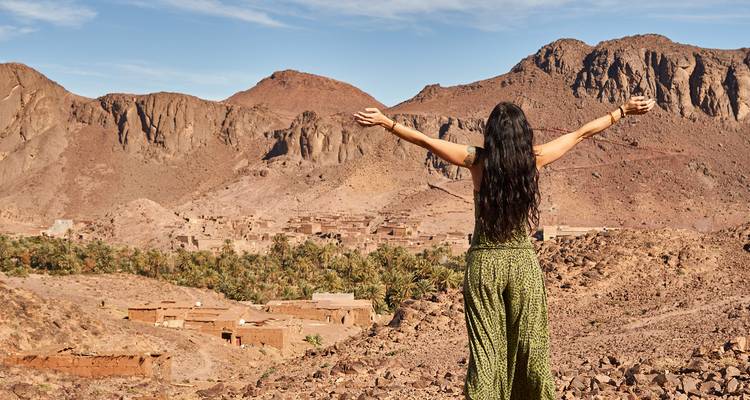 Femme debout avec les bras ouverts dans un paysage désertique rocheux.