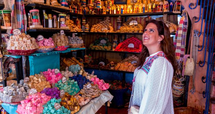 Une femme dans un marché marocain entourée de marchandises teintes colorées.