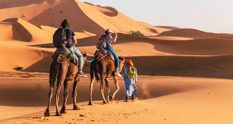 Mensen die op kamelen rijden door een woestijnlandschap.