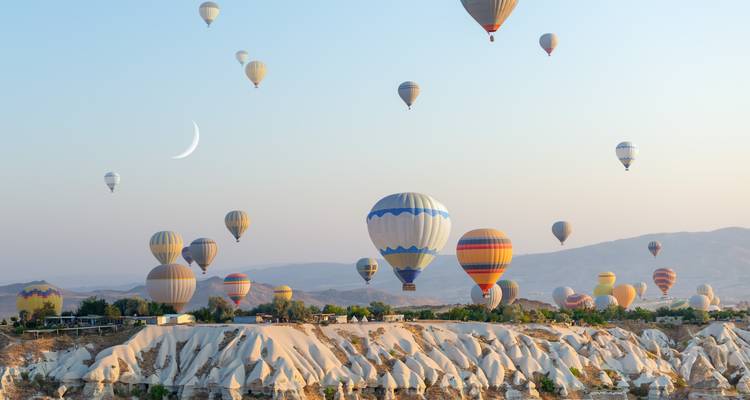 De nombreuses montgolfières flottant au-dessus de formations rocheuses à l'aube.