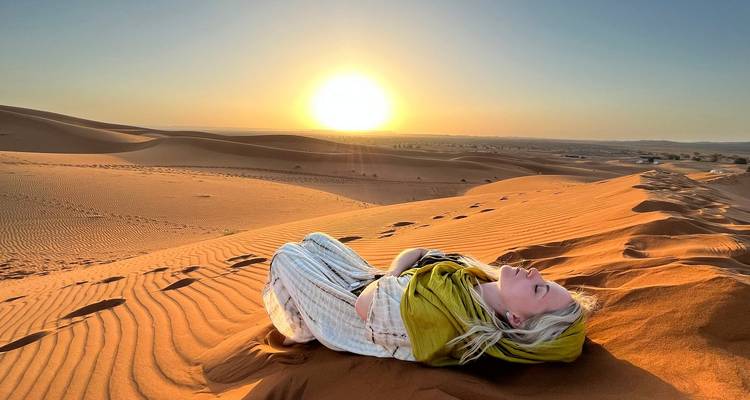 Une personne allongée sur le sable dans le désert au coucher du soleil.