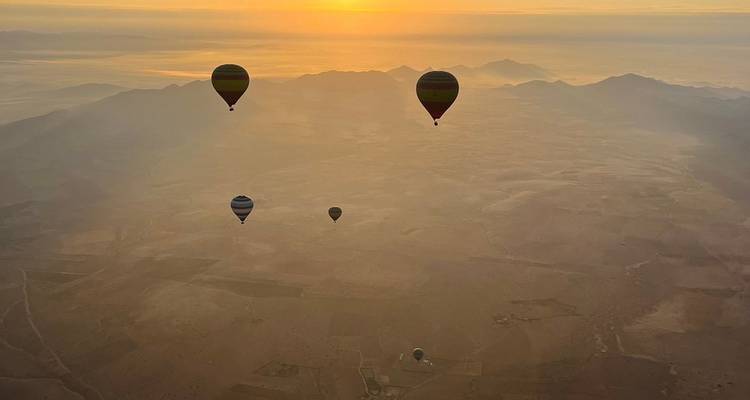 Montgolfières survolant un paysage désertique au lever du soleil.