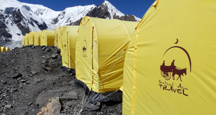 Tentes jaunes alignées avec des montagnes enneigées en arrière-plan.