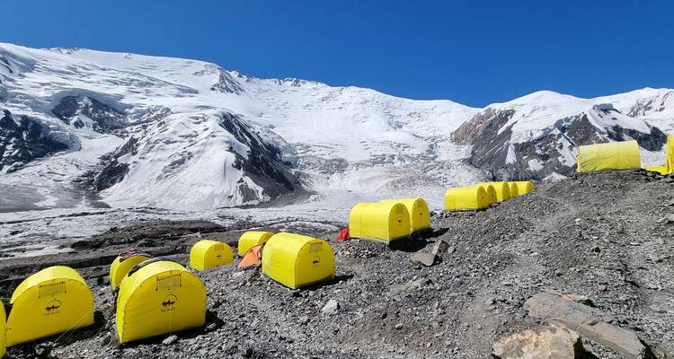 Des tentes jaunes s'étendent à travers un camp de base montagneux rocheux.