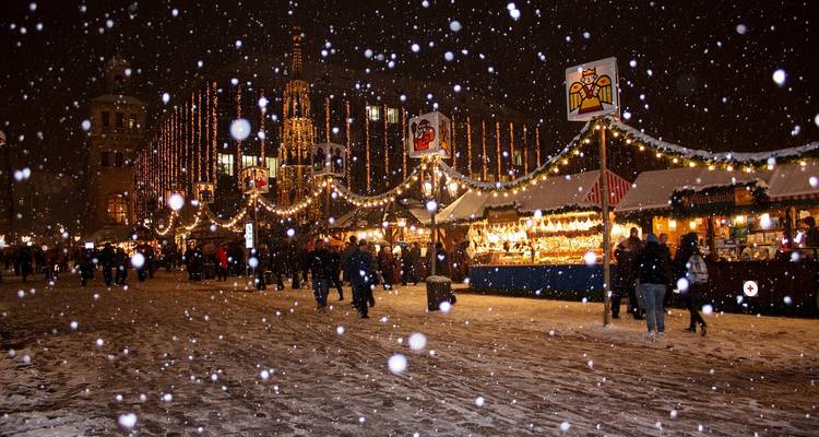 Scène de marché nocturne avec chute de neige, lumières et foules.