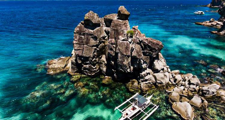 Formation rocheuse dans des eaux turquoise avec un bateau à proximité.
