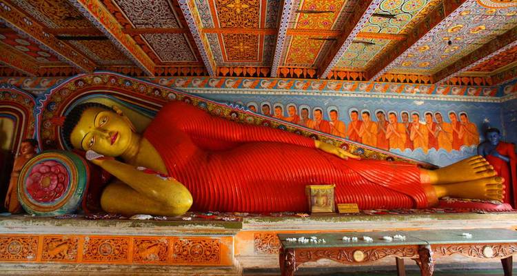 Statue colorée de Bouddha couché dans une salle richement décorée.
