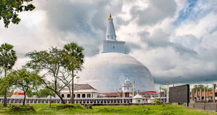 Grand stupa blanc sous un ciel nuageux avec des arbres alentour.