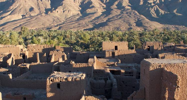 Adobe ruïnes met weelderig groen en bergen.
