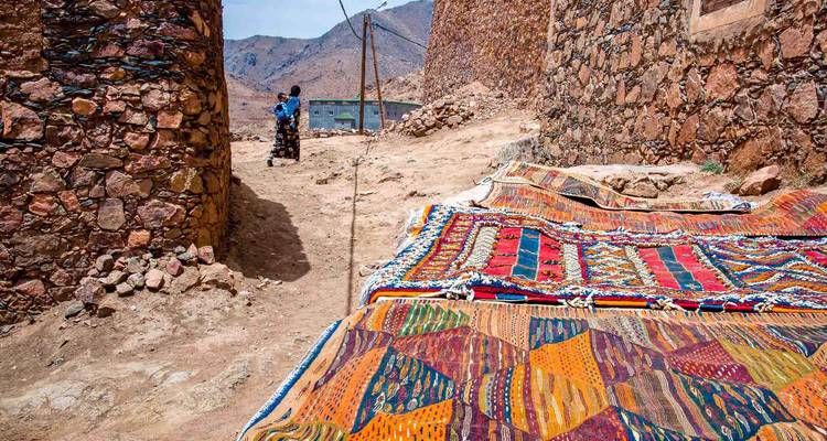 Kleurrijke tapijten tentoongesteld in een stenen steeg.