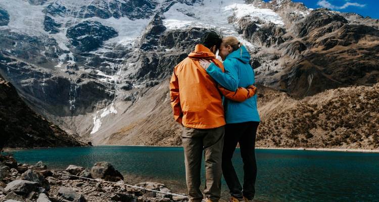 Deux personnes s'embrassant près d'un lac pittoresque avec des montagnes enneigées.