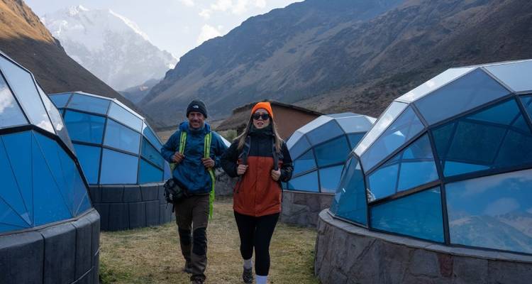Deux personnes marchant parmi des dômes en forme de verre avec des montagnes.
