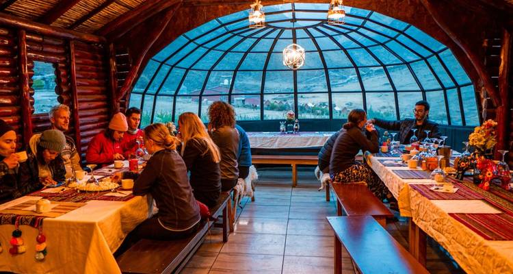 Des personnes dînant à l'intérieur d'un lodge rustique avec un grand plafond de verre.