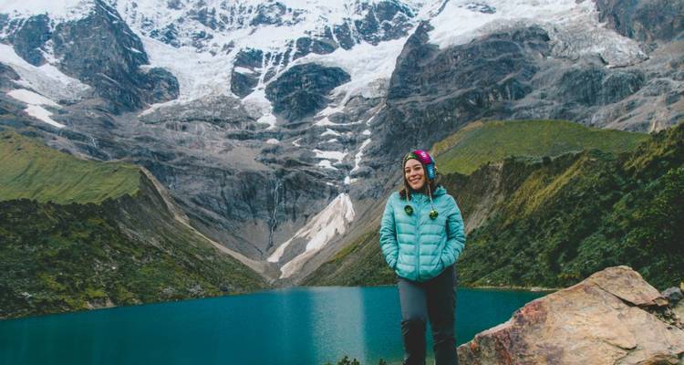 Une personne qui pose près d'un beau lac avec des montagnes.