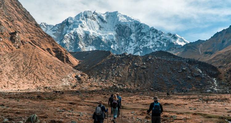 Des randonneurs marchant vers une montagne enneigée sous un ciel dégagé.