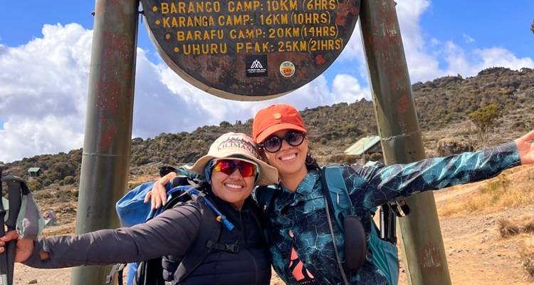 Twee wandelaars die poseren bij een bord dat verschillende kampen aangeeft.