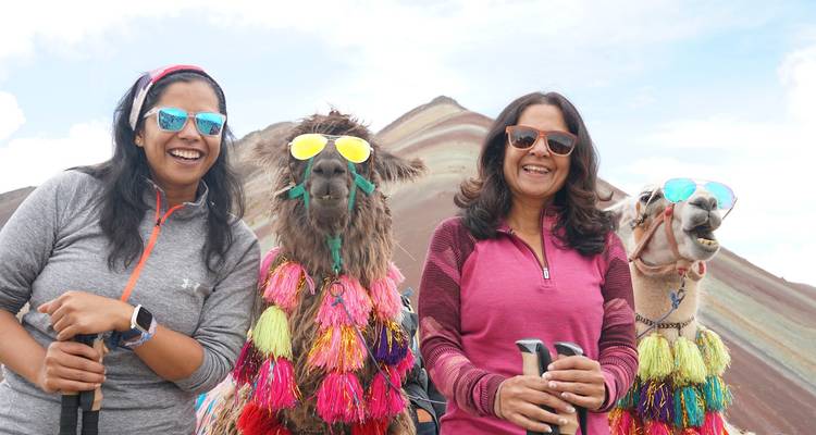 Twee vrouwen en alpaca's die kleurrijke versieringen dragen.