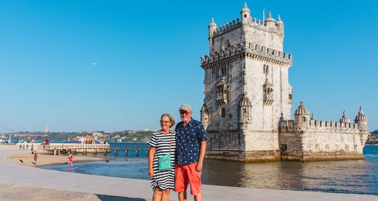 Couple souriant posant près du front de mer avec la Tour de Belém s'élevant derrière eux sous un ciel bleu dégagé