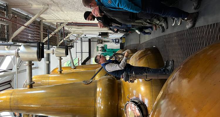 Guide touristique montrant l'équipement à l'intérieur d'une distillerie aux visiteurs.