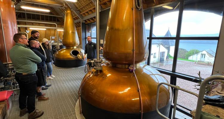 À l'intérieur d'une distillerie avec un grand alambic en cuivre et un groupe d'auditeurs.