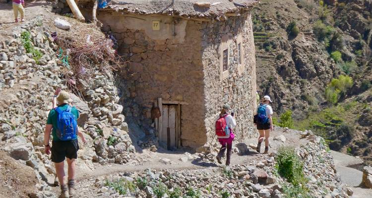 Mensen die een stenen huis in een bergachtig gebied naderen.