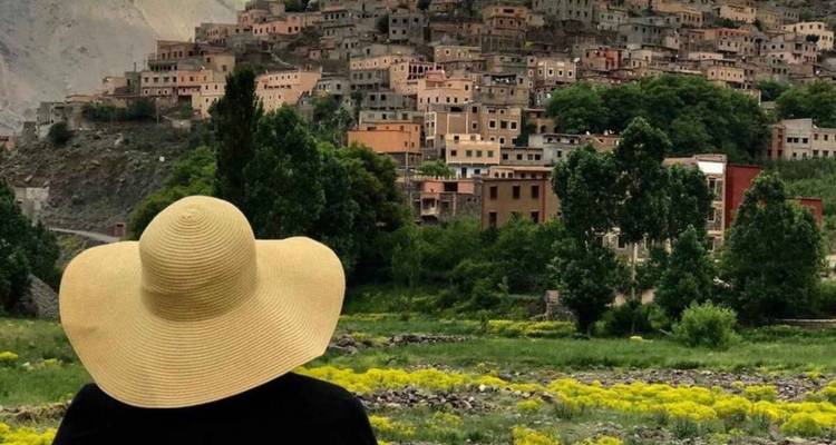 Persoon met een breedgerande hoed die naar een heuvelsdorp kijkt.