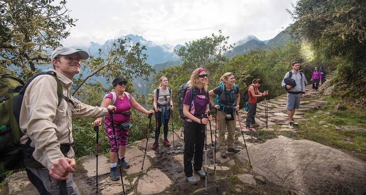 Excursionistas en un sendero de montaña con montañas brumosas al fondo.