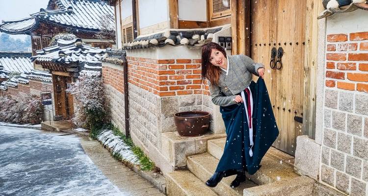 Personne en tenue traditionnelle dans un village coréen enneigé.