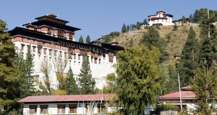 Deux dzongs bhoutanais blancs reposent sur des collines adjacentes entourées de pins.