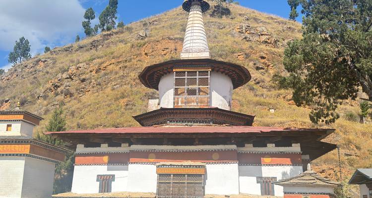 Un grand chorten blanc avec une flèche élancée se dresse au pied d'un versant rocheux bhoutanais.