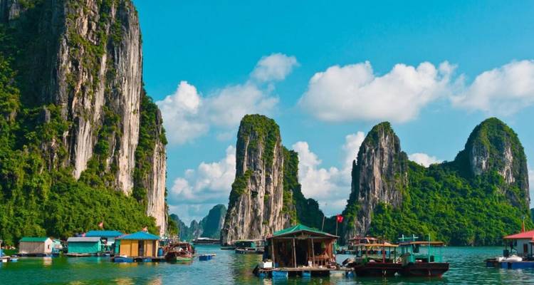 Vue panoramique de karsts calcaires s'élevant depuis des eaux turquoise, avec des maisons flottantes.
