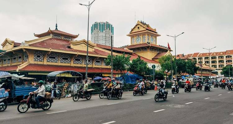 Une rue animée avec des motos et un grand bâtiment de marché.