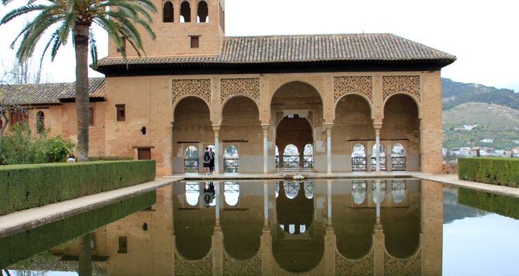 Architecture de style mauresque avec un bassin réfléchissant et des montagnes au loin.