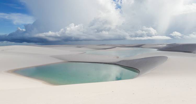White sand dunes with blue lagoons under dramatic skies.