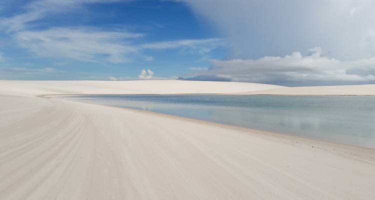 White sand dunes with a serene lagoon and clear skies.