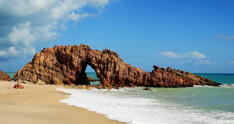 Natural rock arch formation on a beach with ocean waves.