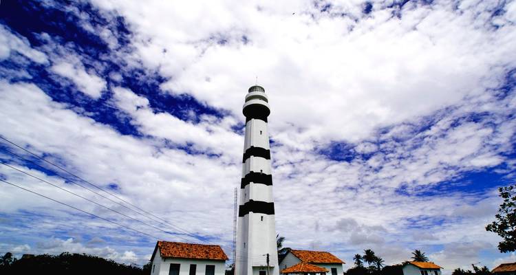 Tall black and white lighthouse with buildings.