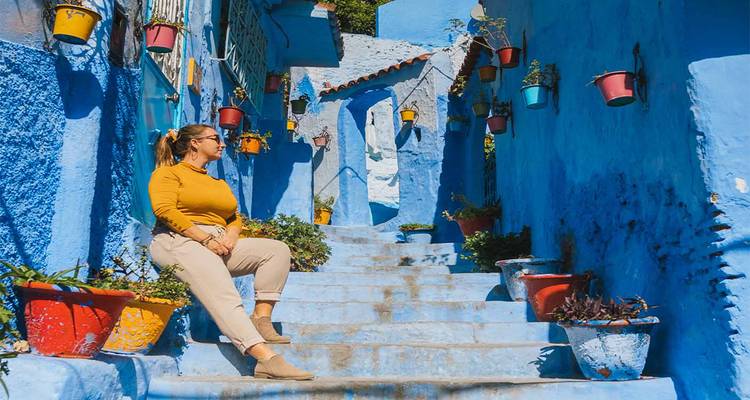 Personne assise sur des escaliers bleus bordés de pots de plantes colorés.