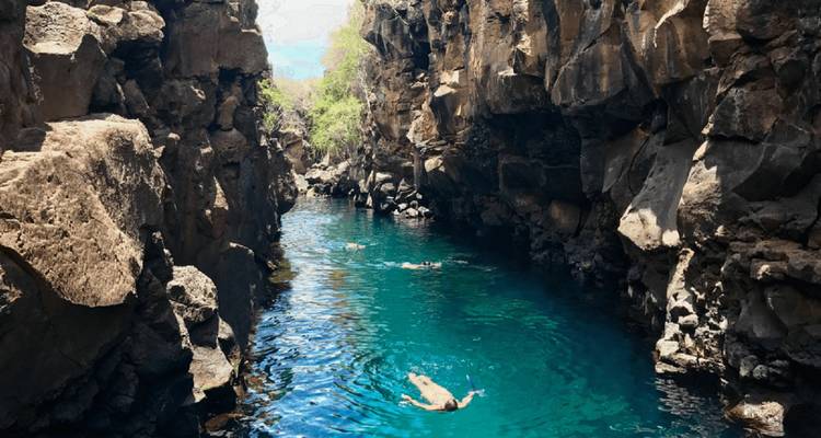 Des gens qui nagent dans un canyon volcanique étroit avec de l'eau turquoise.