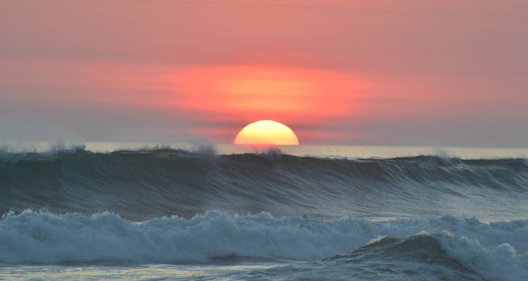 Oceaan zonsondergang met golven die op de voorgrond breken.