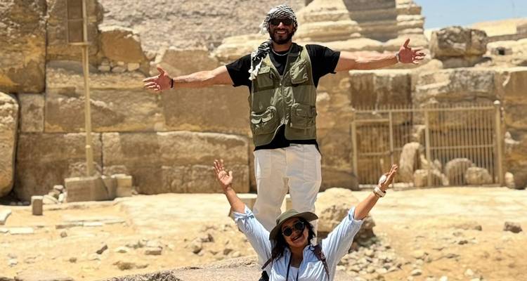 Personnes prenant la pose les bras écartés devant des ruines antiques.