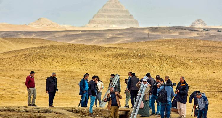 Groupe d'archéologues et de touristes travaillant près d'un site de fouilles avec la Pyramide à degrés en arrière-plan