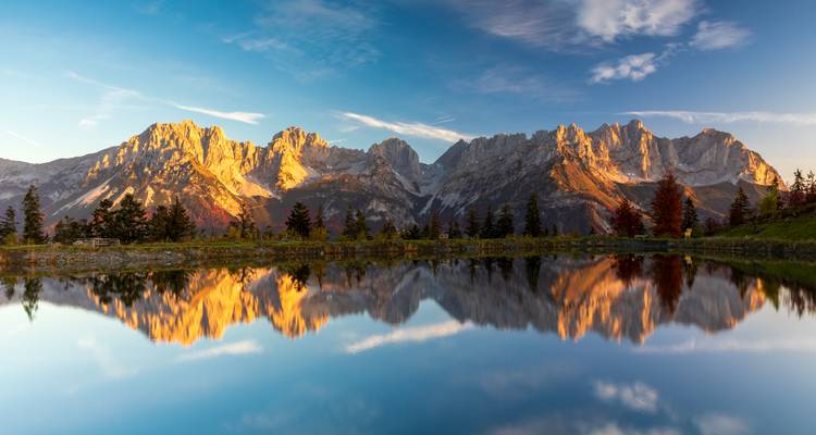 Picos de montañas reflejados en un lago tranquilo al atardecer.