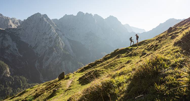Excursionistas en una ladera cubierta de hierba con una cordillera montañosa al fondo.