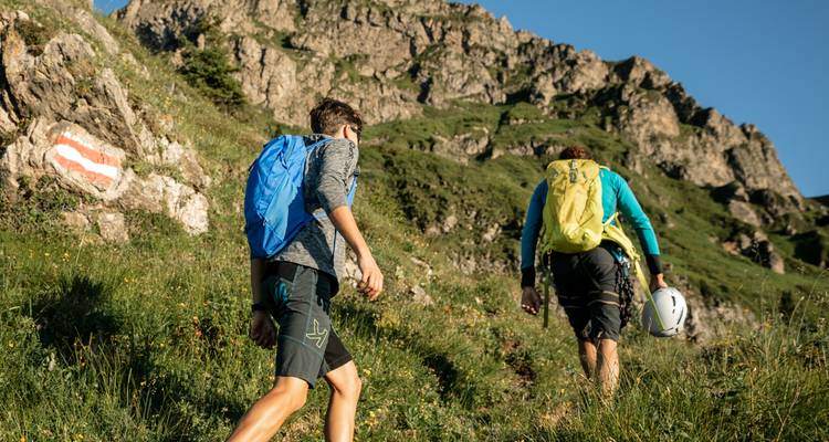 Dos excursionistas ascendiendo una colina cubierta de hierba con acantilados rocosos.